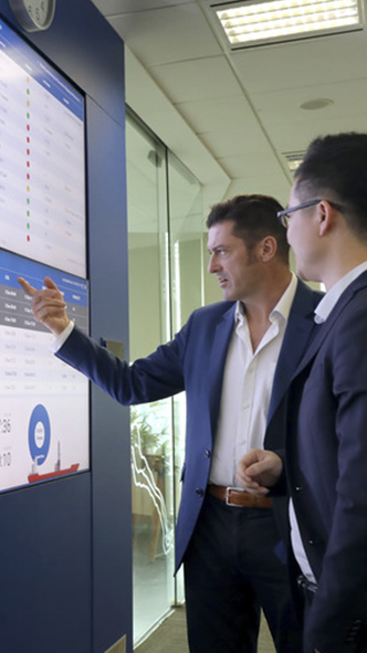 Two men consulting wall screens with data